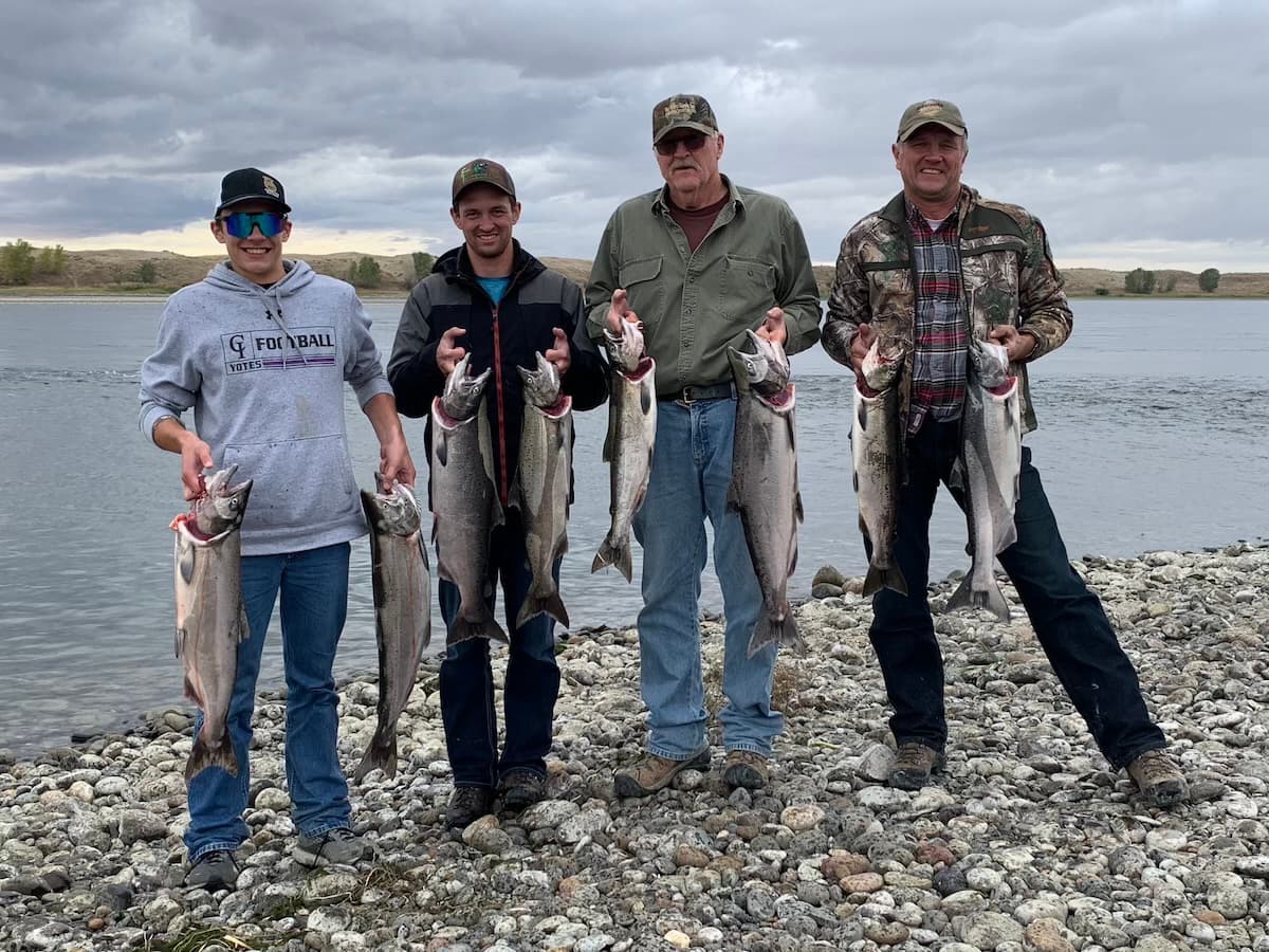Four anglers displaying salmon catch on Columbia River shore in Washington