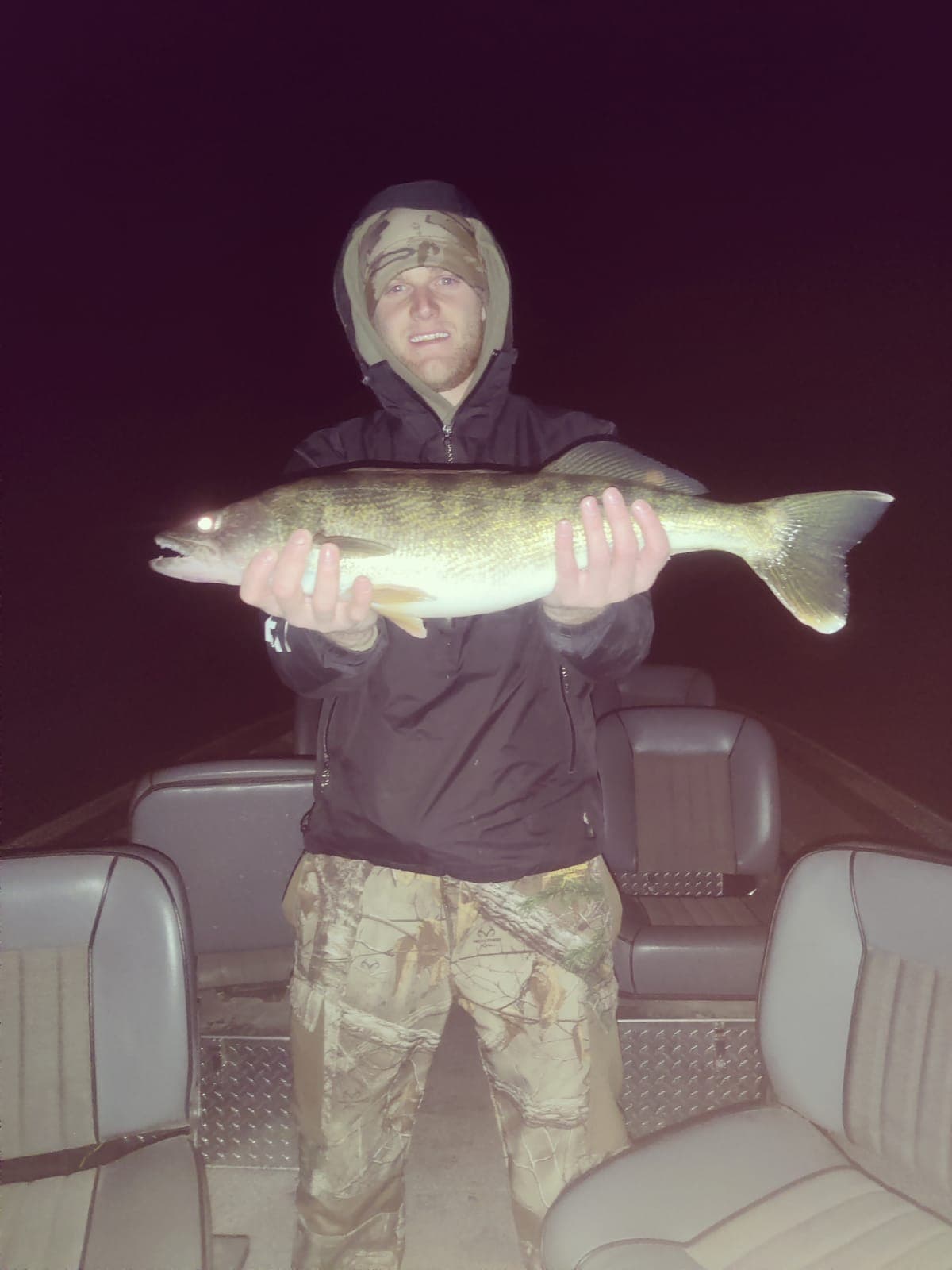 Angler holding large walleye at night on guided fishing boat